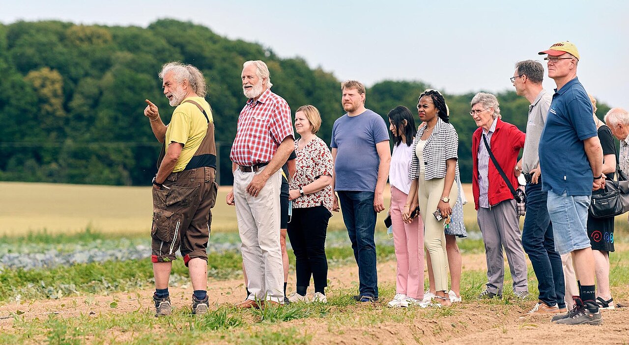Eine Menschengruppe steht auf einem Feld und schaut in die Ferne