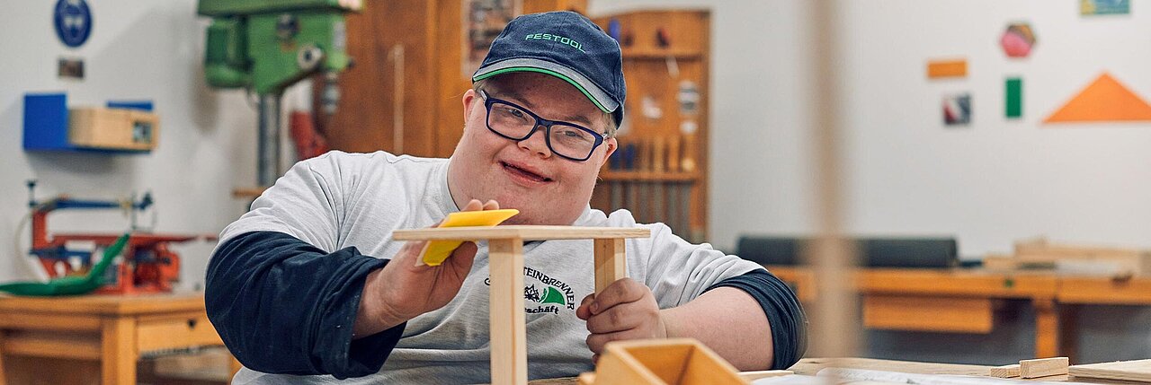 Ein junger behinderter Mann schleift ein Holzteil in der Werkstatt